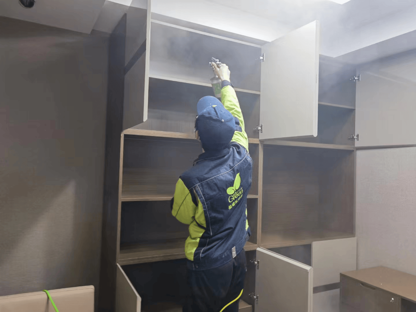 客厅施工时，一名施工人员站在梯子上，对天花板吊灯附近的空气进行除醛喷雾，另一名施工人员在下方协助。
